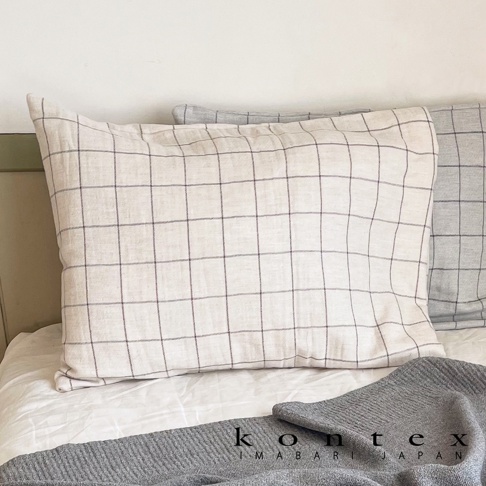 GRAPH 草木染格紋有機棉枕套，米白色枕套上印有細緻的深色網格紋，材質柔軟，搭配灰色格紋枕套和灰色毛毯，營造清新自然的臥室氛圍。