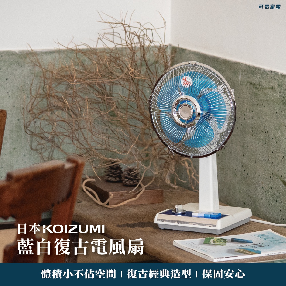 日本KOIZUMI藍白復古電風扇，10吋扇葉，銀色金屬網罩，白色支架與底座，底座有多段開關及藍色按鈕，擺放於木質桌面，背景有乾燥樹枝與松果裝飾。