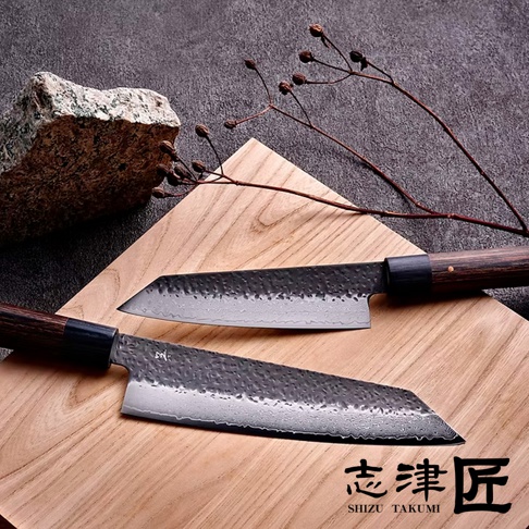 玄 / Bunka 文化刀19cm，兩把錘紋鋼刀刃，深棕色木質手柄，置於木質砧板上，背景為灰色石材與乾燥枝條。