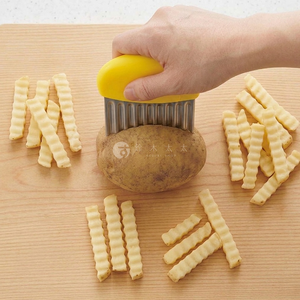 一隻手握著黃色握把的波浪造型切刀，正在切削一顆置於木質砧板上的馬鈴薯，砧板周圍擺放著多根已經切好的波浪狀薯條，整體呈現出廚房備料的情境。