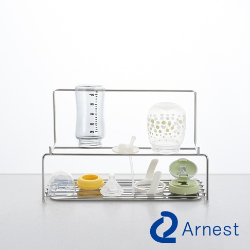 Arnest 品牌雙層不鏽鋼奶瓶瀝水架，上層擺放有刻度的玻璃奶瓶和印有綠色圓點的玻璃奶瓶，下層擺放有奶瓶蓋、黃色奶嘴環、奶嘴、奶瓶架和綠色奶瓶蓋。