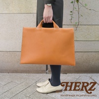 手提駝色簡約皮革公事包，搭配米白色牛津鞋，包包上有HERZ字樣。