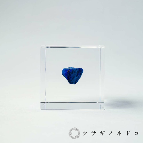 方形透明壓克力塊中，懸浮著一塊深藍色、帶有不規則紋理的青金岩礦石。