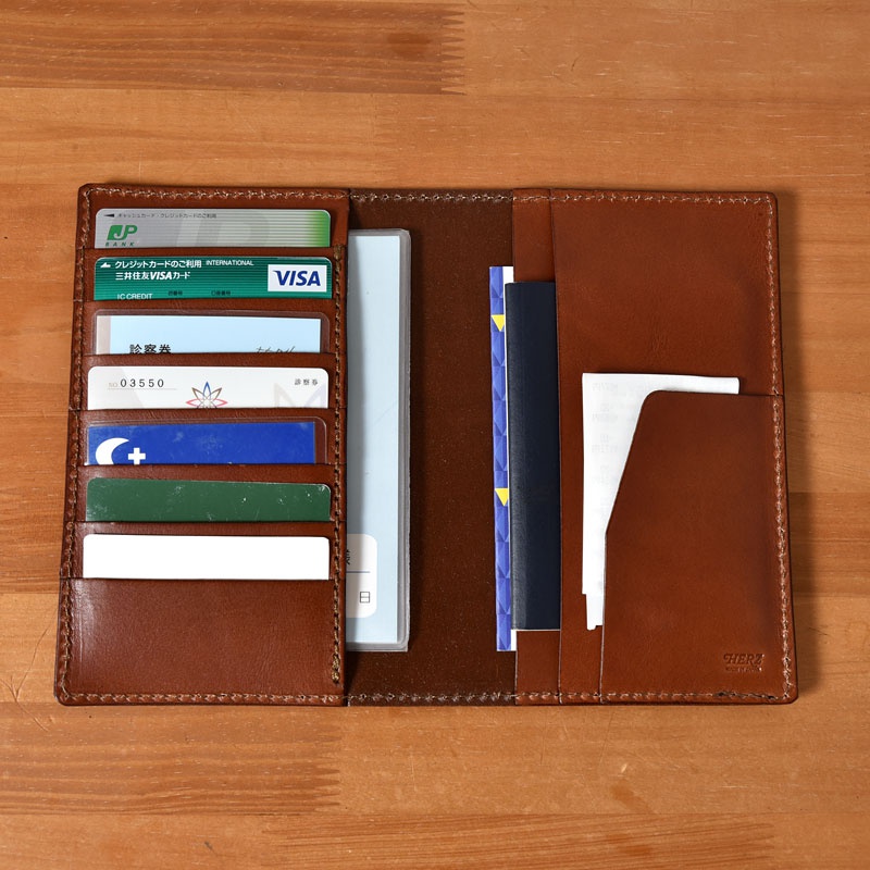 棕色皮革多用途收納長夾，內部有數個卡槽，插有信用卡、診斷券等卡片，以及文件和護照。皮革表面光滑，縫線整齊。