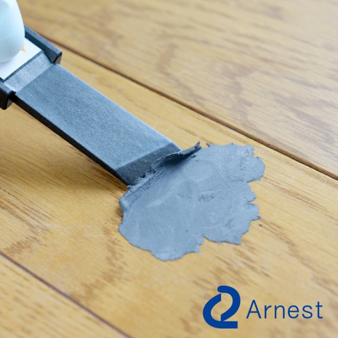 灰色刮刀正在木質地板上刮除灰色填充物。