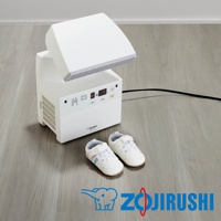 白色多功能智慧烘乾機，設有 LED 顯示螢幕和控制按鈕，上方頂蓋可向上傾斜，旁邊地面放著一雙白色嬰兒鞋，鞋上有粉色和藍色條紋裝飾。