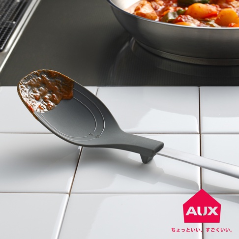 灰色不沾桌拌炒量匙，匙面有刻度線，帶有少許醬料，匙柄為銀色金屬材質。