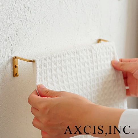 黃銅單桿毛巾架，固定在白色紋理牆壁上，一塊白色格紋毛巾被兩隻手掛在桿上。