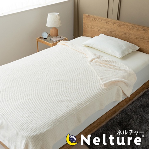 象牙白紋理柔暖毯鋪陳在單人床上，毯子表面帶有細緻的條紋紋理，一角搭著一條同色系的毯子，搭配木質床頭板和白色枕頭。