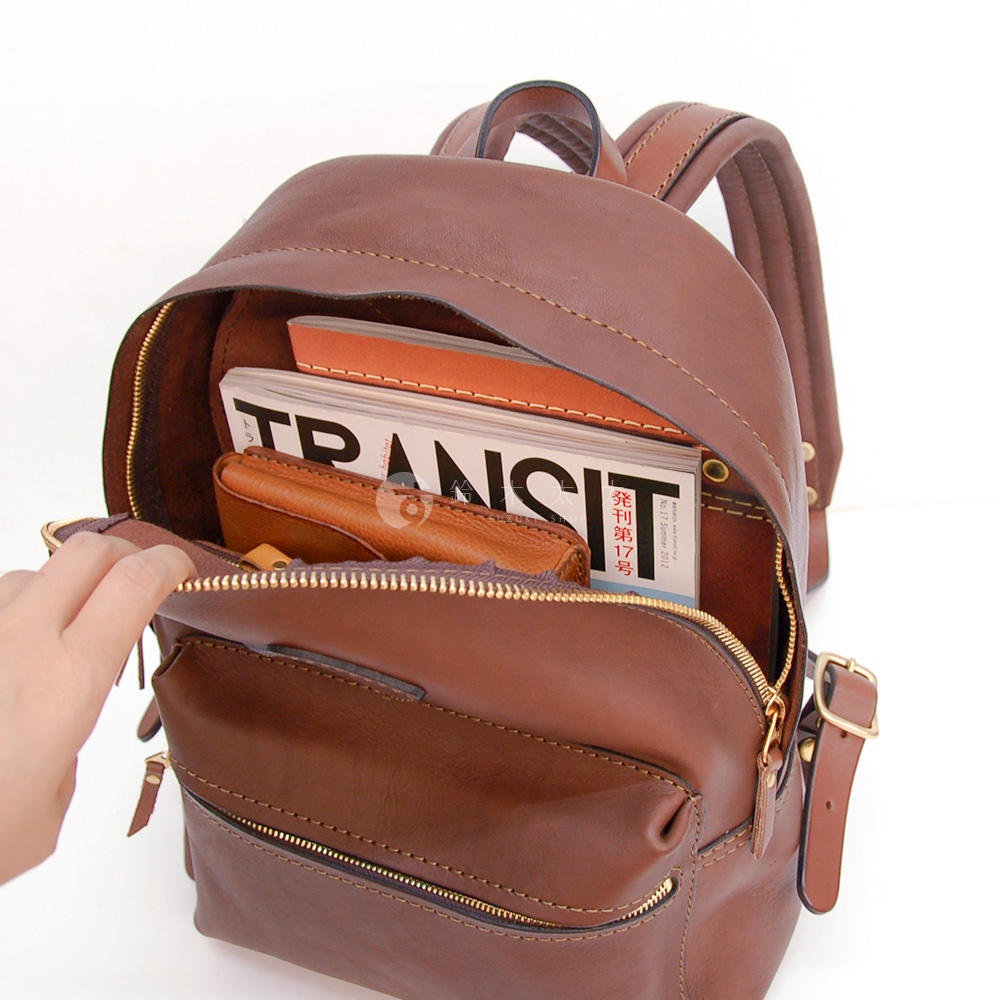 職人手作皮革後背包，咖啡棕色，主隔層打開，內有雜誌和皮夾，拉鍊及肩帶細節。