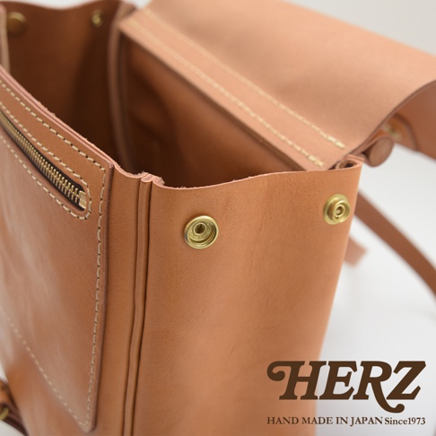 職人手作皮革屋瓦風後背包R-15，採用淺棕色皮革，帶有金屬壓扣和拉鍊細節，縫線清晰，展現日式簡約風格。