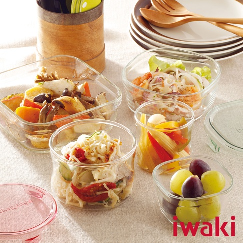 多個透明耐熱玻璃圓形和方形保鮮盒，內含不同種類的醃漬蔬菜、沙拉和水果，置於淺色桌布上。