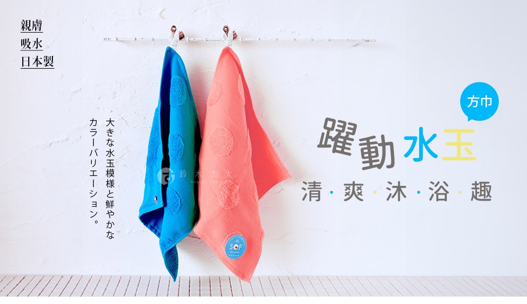 兩條紗布方巾，一條為鮮豔的藍色，另一條為珊瑚粉色，皆帶有大圓點紋飾，掛在白色牆面上。