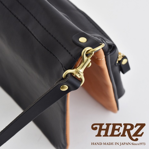 職人手作皮革翻轉雙色直式斜背包，黑色皮革外層搭配淺棕色內層，配有黃銅色金屬扣環及拉鍊。