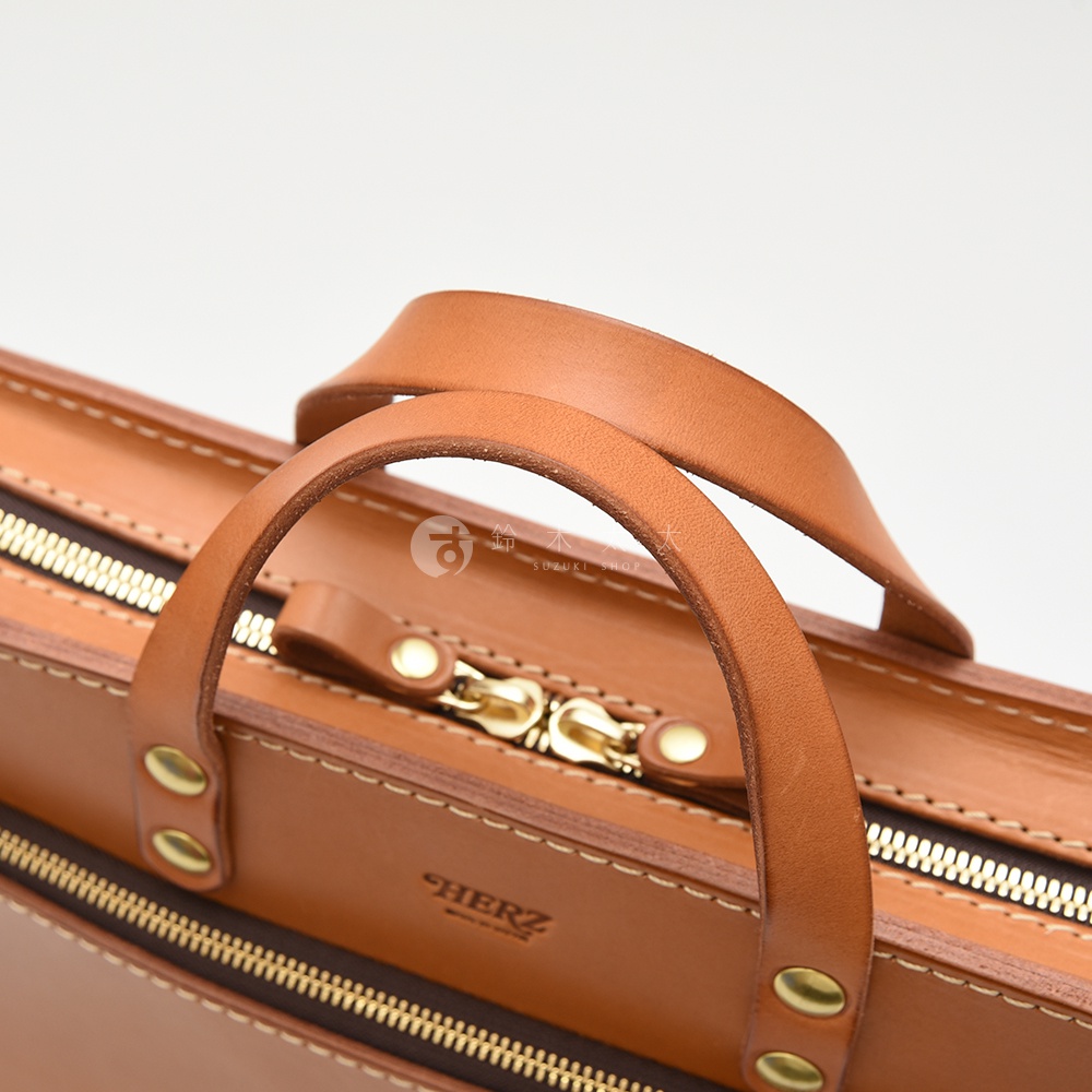 職人手作皮革兩用商務公事包，採用溫潤的棕褐色皮革，搭配復古金色拉鍊與铆釘。包款設有兩個皮革提把，做工精緻，展現質感。