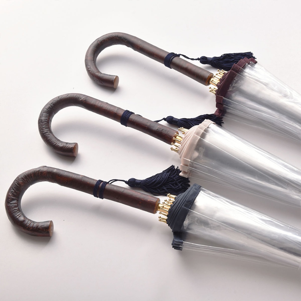 三把職人高級樺木透明傘，傘柄為彎曲的木質，繫有深藍色流蘇。傘面為透明材質，傘骨頂端有金屬配件，傘邊分別為深藍、淺米色和酒紅色。