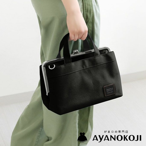 一位女性穿著淺綠色褲裝，手提一只黑色橫式口金手提包，包包上有品牌標籤 AYANOKOJI。