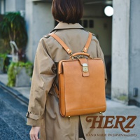 職人手作皮革杜勒斯商務後背包，棕褐色牛皮革材質，方正造型，配有金屬鎖扣與提把，可肩背或後背。