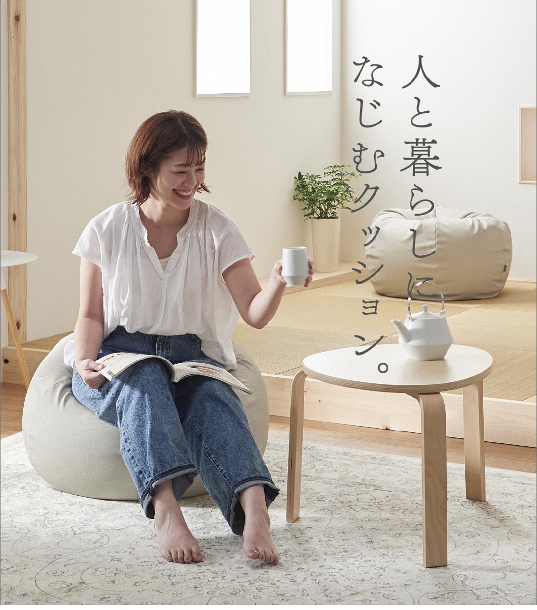 女性坐在淺米色皮革懶骨頭沙發上，手持杯子，腳邊放著書本。沙發旁有白色茶壺和木製茶几。