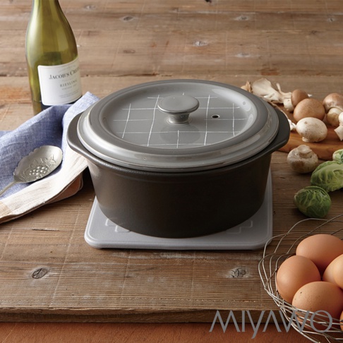 深棕色陶土湯鍋，配有淺灰色格紋鍋蓋，鍋蓋中央有把手和透氣孔。湯鍋放置在淺灰色鍋墊上，背景有酒瓶、餐巾、湯匙、蘑菇和雞蛋。