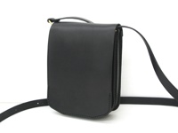 黑色皮革翻蓋直式單肩包，附有可調式肩帶和金色搭扣。包體線條簡潔，材質光滑，邊緣縫線工整。