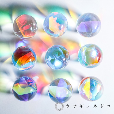 九顆圓形透明玻璃稜鏡球，內部呈現彩虹般的光影折射，有紅色、橘色、黃色、藍色、紫色等色彩，球體表面光滑，背景為模糊的彩色光暈。