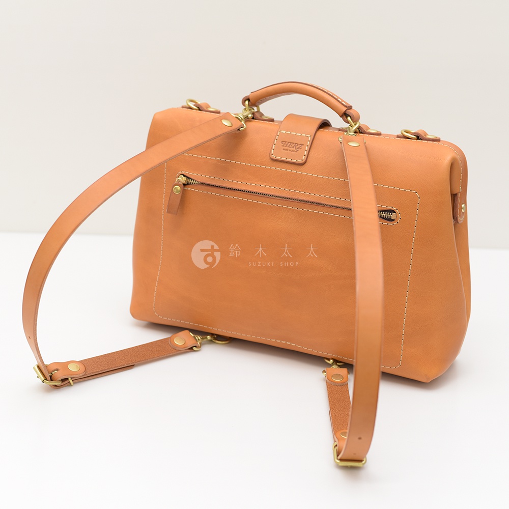 職人手作的軟式杜勒斯包，採用天然皮革製成，呈現溫潤的焦糖棕色。包款背面有拉鍊口袋，並配有可拆卸的皮革肩帶，可依需求轉換為後背包或側背包。精緻的手縫車線與復古金屬配件，展現質感。