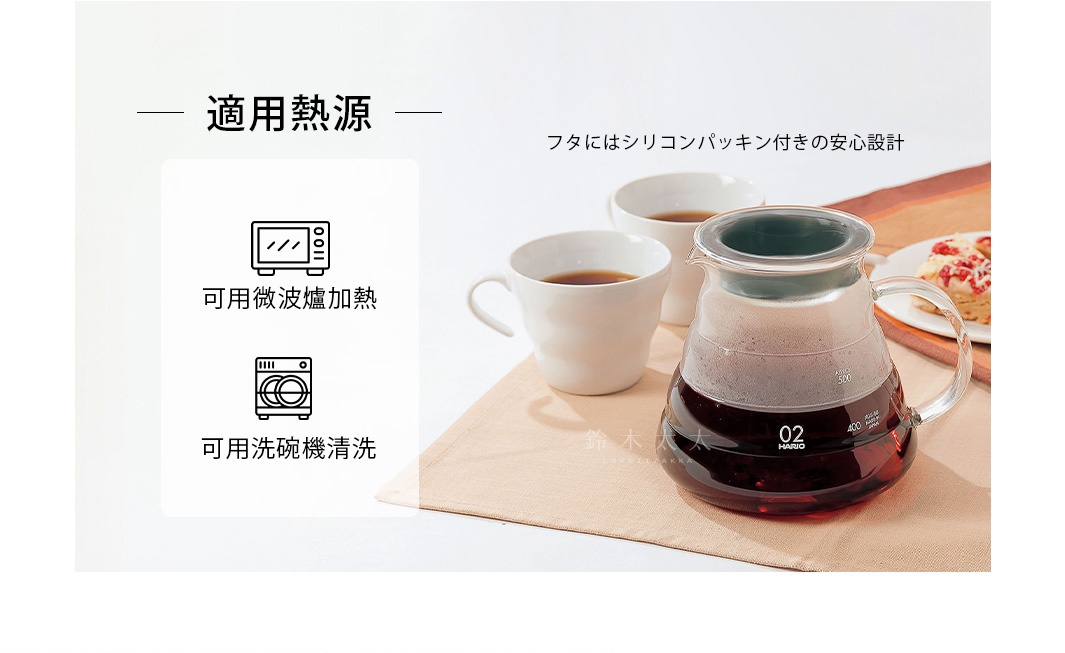 透明玻璃咖啡壺，帶有手柄和刻度線，壺內裝有深棕色液體。旁邊擺放著兩個白色咖啡杯，其中一個裝有咖啡。背景是淺米色布料。