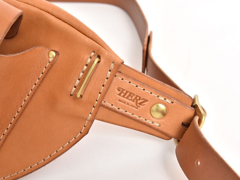 職人手作皮革斜背包，採用自然色皮革，精緻縫線，配有黃銅扣環和品牌標誌。