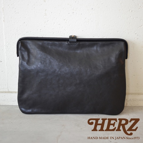 職人手作黑色皮革Organ手拿包，簡約設計，帶有金色金屬扣環，展現天然皮革的紋理質感。