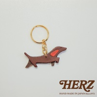 職人手作皮革狗狗造型鑰匙圈，深棕色皮革製成，裝飾有紅色皮革斑紋，搭配金色鑰匙圈與扣環。