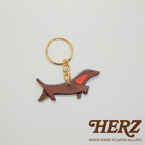 職人手作皮革狗狗造型鑰匙圈，深棕色皮革製成，裝飾有紅色皮革斑紋，搭配金色鑰匙圈與扣環。