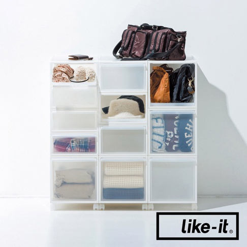like-it 品牌的可堆疊抽屜式收納箱，箱內收納著衣物、帽子和包包，最上方擺放著一個深色的大旅行袋。