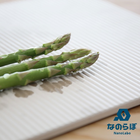 淺灰色條紋珪藻土置物墊上放著三支帶有水珠的綠色蘆筍。