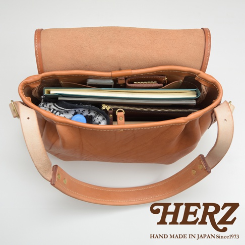 職人手作皮革大容量扣環郵差包，棕色皮革，內有手機、筆記本、錢包、水瓶和衣物。