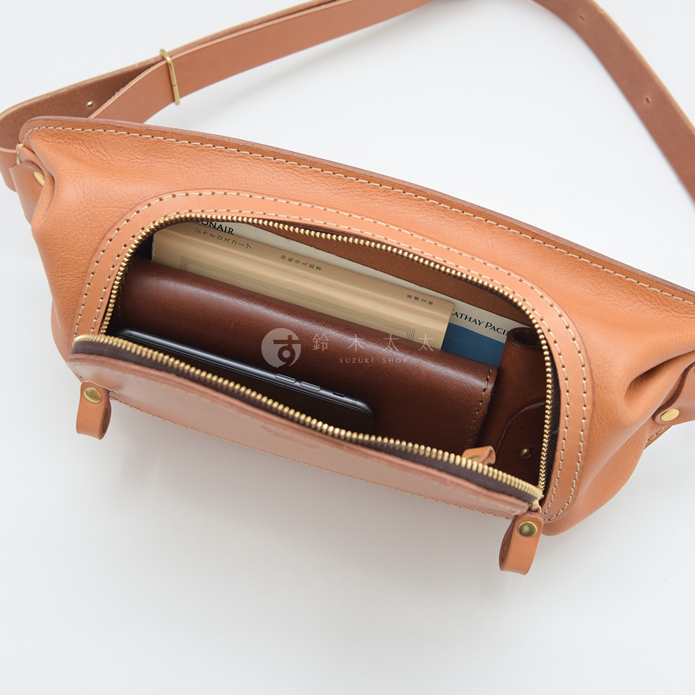 一個日本製HERZ品牌棕色皮革拉鍊斜背包，包包內有手機、錢包和兩本書，其中一本書上有SUZUKI SHOP字樣。