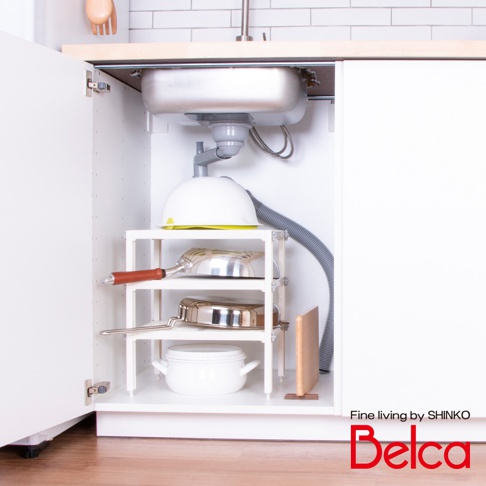 白色三層迷你收納架，架上擺放著鍋子、平底鍋和湯鍋。收納架位於廚房水槽下方，周圍有水管和白色櫥櫃。