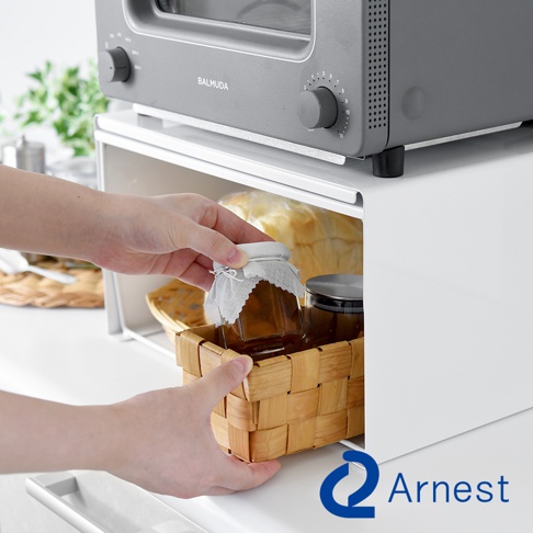 灰白色金屬廚房收納架，上方放置灰色烤箱，下方收納籃內有玻璃瓶裝物，由雙手放入。