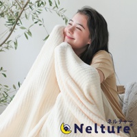 一位年輕女子被奶油色柔軟毛毯包裹，毛毯有著細緻的條紋織紋。