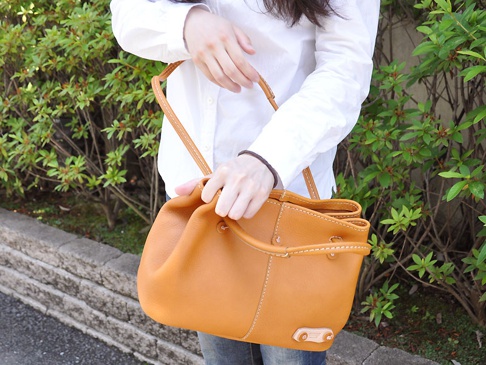 棕色皮革托特包，有可調式提把和肩帶，包身有縫線細節，底部有品牌標誌。