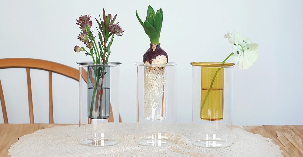 AXCIS PINO 雙層可拆玻璃花瓶-高款，展示了三款分別擺放著紫色花束、水耕植物和白色花朵的玻璃花瓶，瓶身呈現雙層設計，其中一個瓶身有琥珀色。