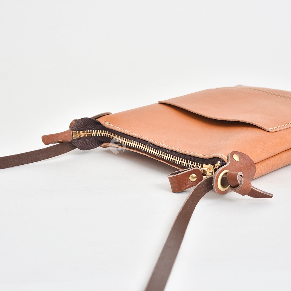 職人手作皮革直式隨身單肩包，淺棕色皮革，配有黃銅色拉鍊和皮革繫帶，簡約設計。