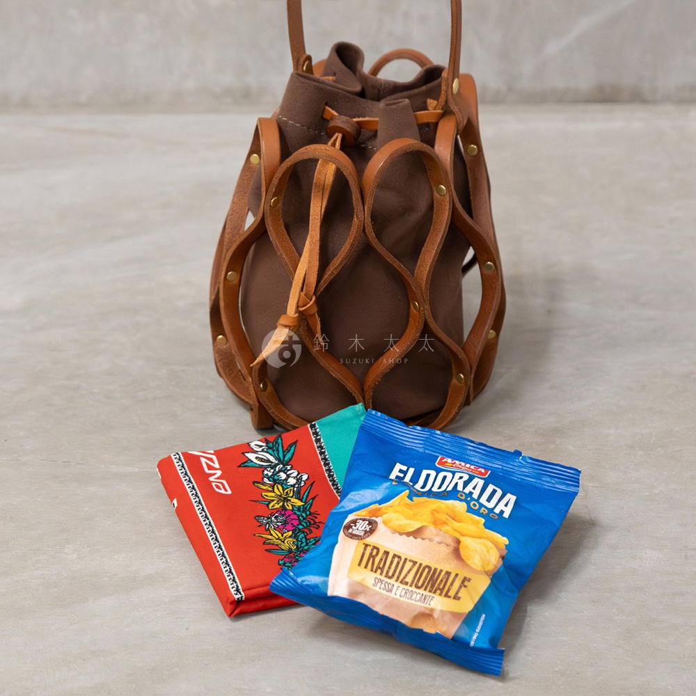 日系職人手作皮革編織水桶包，搭配兩款小點心零食，一款紅色花卉圖案，一款藍色包裝的「EL DORADA TRADIZIONALE」薯片。