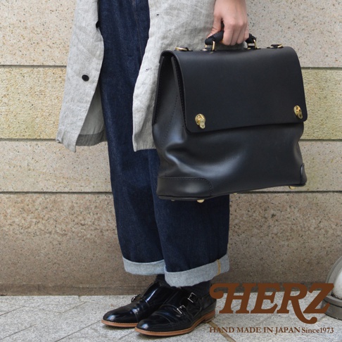 黑色皮革波士頓包，有金色金屬扣飾，頂部有提把，款式簡約，適合旅行或商務場合。