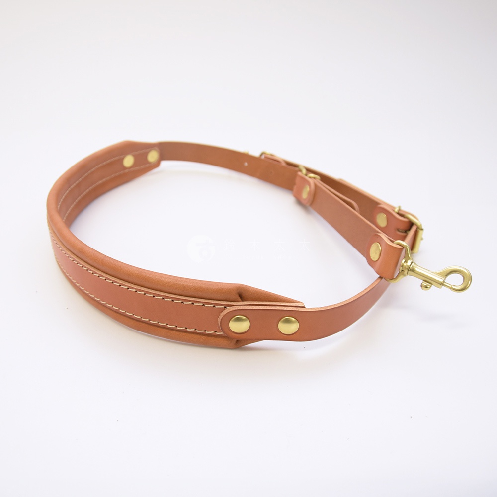 職人手作皮革加厚減壓肩背帶，顏色為淺棕色，材質為皮革，配有銅色金屬扣環和鉤扣，肩墊部分有縫線裝飾。