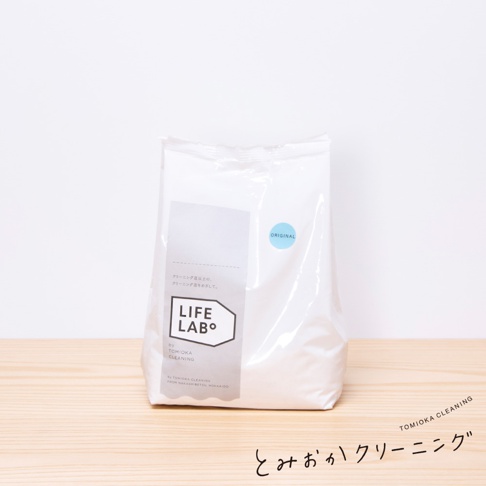 白色補充包洗衣粉，正面有淺灰色標籤，標籤上有「LIFE LAB°」字樣和日文說明。右側有一個圓形藍色貼紙，上面寫著「ORIGINAL」。產品置於木質檯面上，背景為白色。