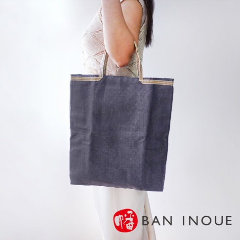 一款深灰色蚊帳棉織隨身購物袋，袋身紋理清晰，提把處有黃、白、金三色條紋裝飾。