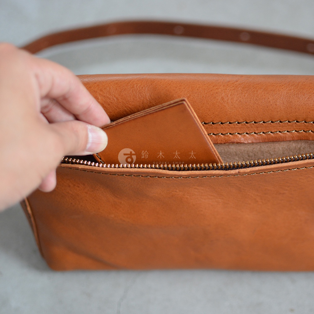 職人手作皮革包，棕色皮革材質，拉鍊細節，手部正在從拉鍊口袋中取出卡片。