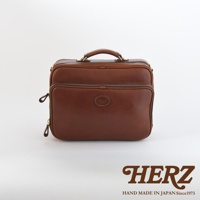 咖啡色皮革製成的手提公事包，中間有圓形品牌標誌，雙拉鍊設計，頂部有提把，兩側有可拆卸的肩帶固定點。