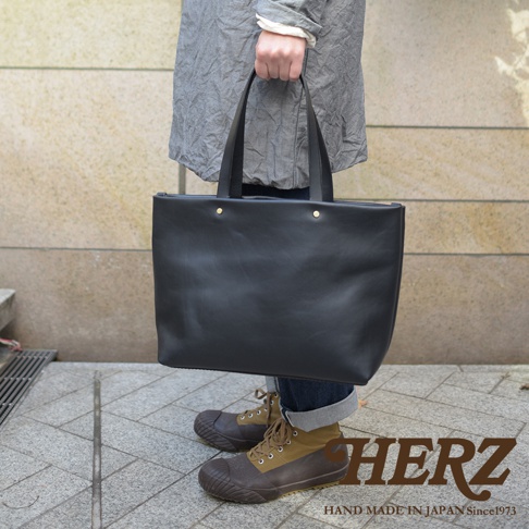 黑色皮革極簡托特包，以簡約的四口袋設計，展現職人手作質感。皮革材質光滑，包身線條俐落，配有雙提把。